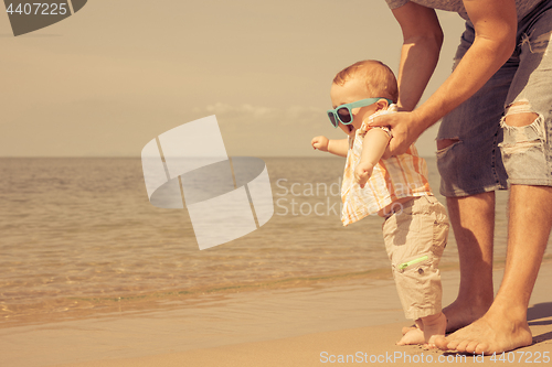 Image of Father and baby son playing on the beach at the day time.