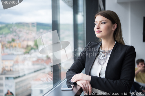 Image of Elegant Woman Using Mobile Phone by window in office building