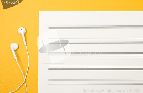 Image of Earphones and blank music sheet on yellow background