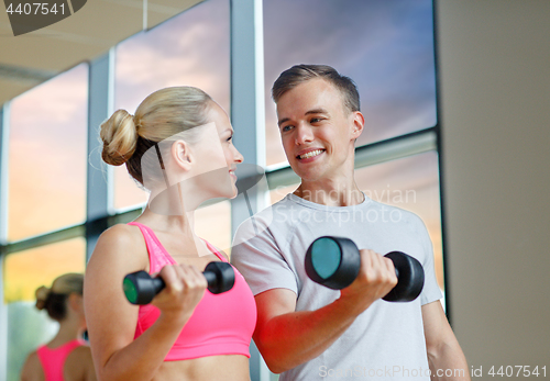 Image of smiling young woman with personal trainer in gym