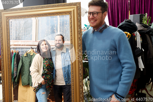 Image of happy friends at mirror at vintage clothing store