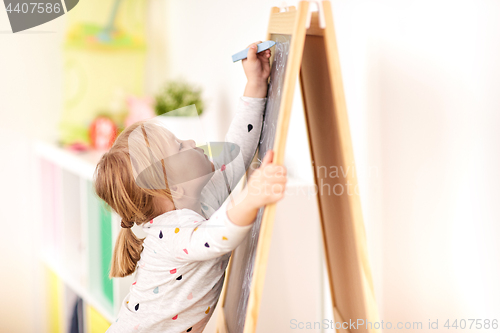 Image of happy little girl drawing on chalk board at home