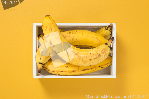 Image of Ripe bananas in a box on bright yellow background