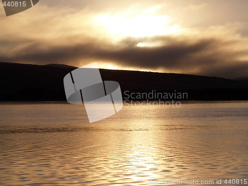 Image of golden sunrise through clouds over water