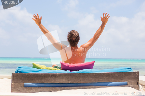 Image of Relaxed man in luxury lounger, arms rised, enjoying summer vacations on beautiful beach.