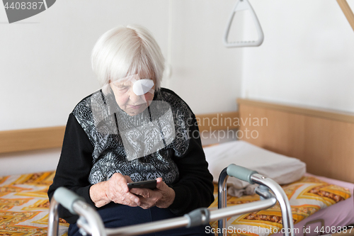 Image of Lonley elderly 95 years old woman sitting at the bad using modern mobile phone.