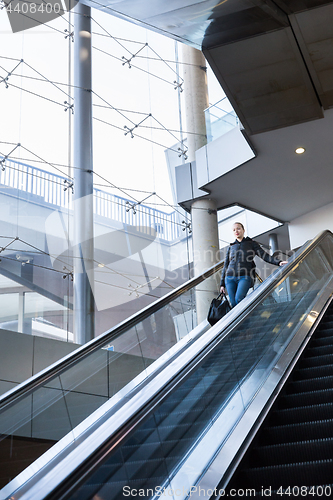 Image of Businesswoman with large black bag and mobile phone ascending on escalator.