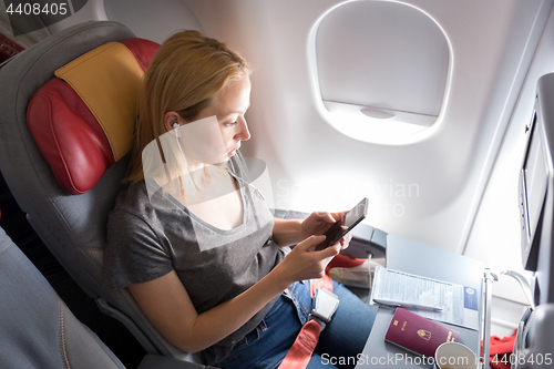 Image of Woman listening to music on smart phone on commercial passengers airplane during flight.