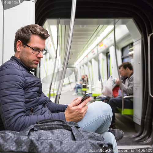 Image of Male commuter reading from mobile phone screen in metro.