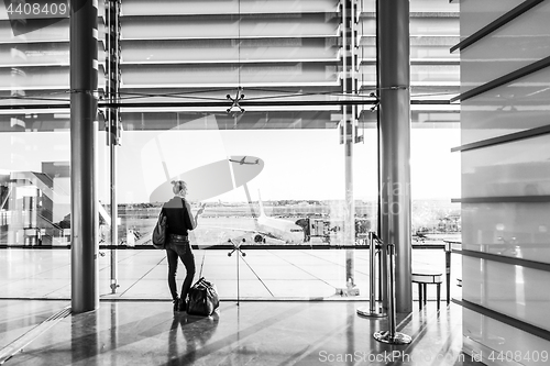 Image of Young woman waiting at airport, looking through the gate window.