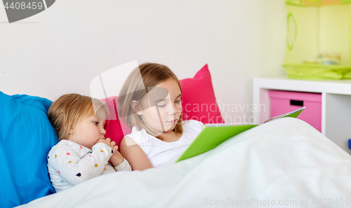 Image of little girls or sisters reading book in bed