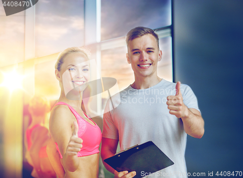 Image of smiling young woman with personal trainer in gym