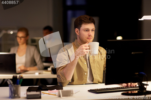 Image of man with laptop and coffee working at night office