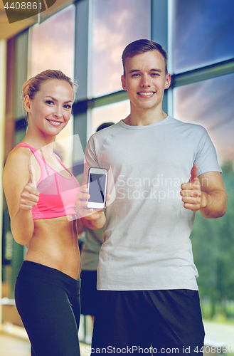 Image of smiling young woman with personal trainer in gym