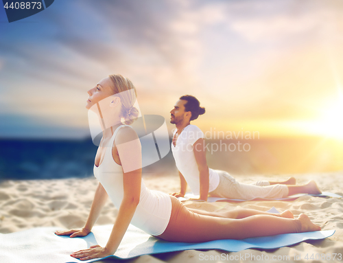 Image of couple doing yoga and cobra pose on beach