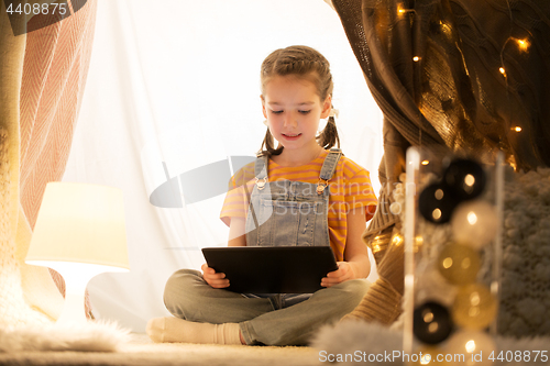 Image of little girl with tablet pc in kids tent at home