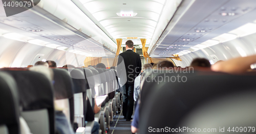 Image of Interior of commercial airplane with steward walking the aisle.