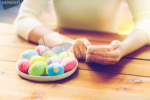 Image of close up of hands with easter eggs and smartphone