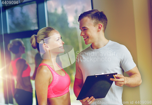 Image of smiling young woman with personal trainer in gym