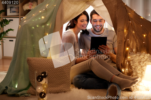 Image of happy couple with tablet pc in kids tent at home