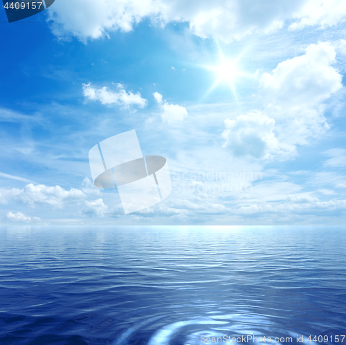 Image of blue sky with some clouds and the sun over the ocean