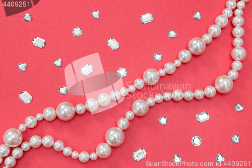 Image of Pearl necklace and shiny gems on pink background