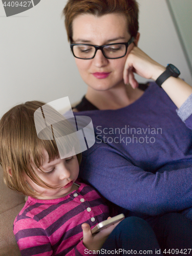 Image of mother and her cute little daughter are using a mobile phone