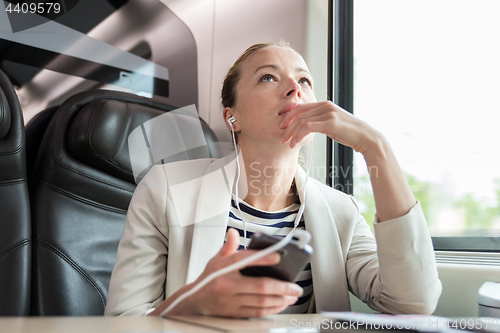 Image of Thoughtful businesswoman listening to podcast on mobile phone while traveling by train.