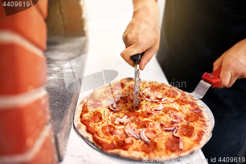 Image of cook hands cutting pizza to pieces at pizzeria