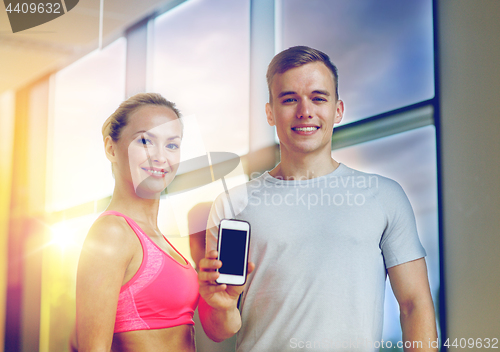 Image of smiling young woman with personal trainer in gym