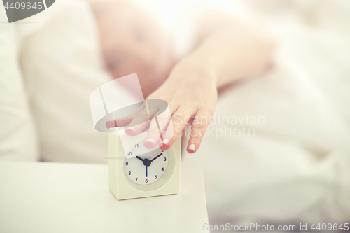 Image of close up of woman with alarm clock in bed at home