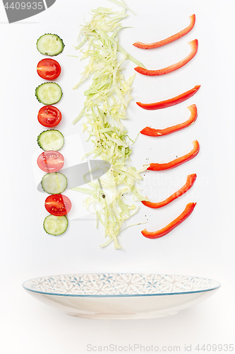 Image of The salad bowl in flight with vegetables: tomato, cucumber, cabbage on white background