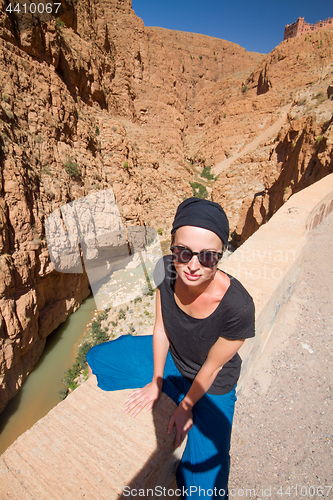 Image of Image of female tourist relaxing on winding road bank in Dades Valley, Atlas mountains, Morocco.