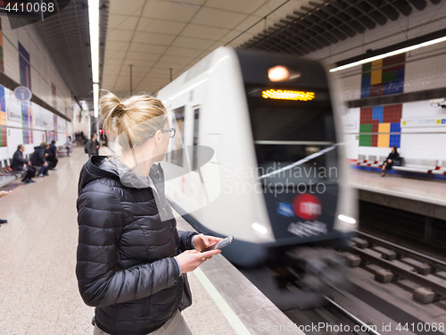 Image of Woman with a cell phone waiting for metro.