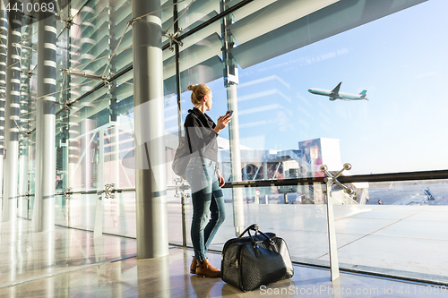 Image of Young woman waiting at airport, looking through the gate window.