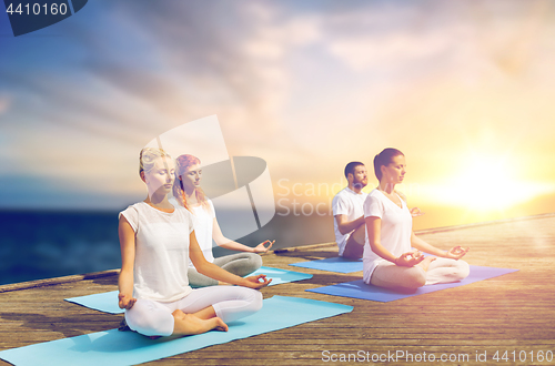 Image of people meditating in yoga lotus pose outdoors