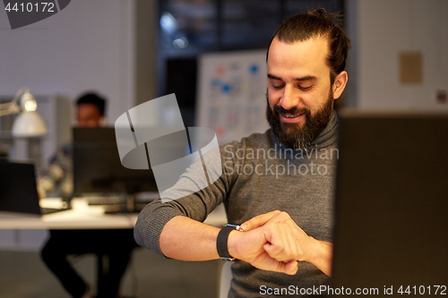 Image of creative man with smartwatch at night office