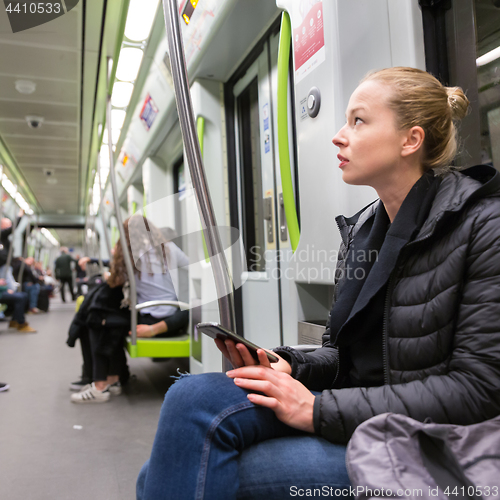 Image of Young girl with mobile phone traveling on metro.