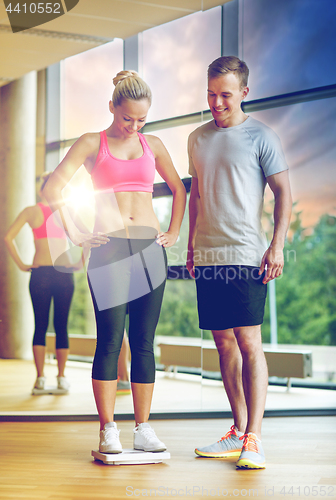 Image of smiling man and woman with scales in gym