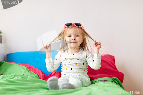 Image of smiling little girl with sunglasses on bed at home