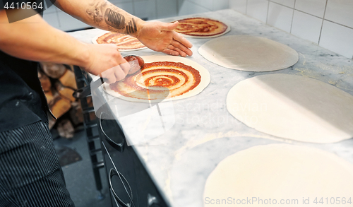 Image of cook applying tomato sauce to pizza at pizzeria