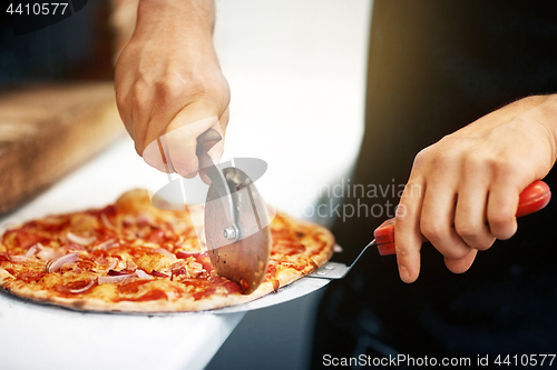 Image of cook hands cutting pizza to pieces at pizzeria