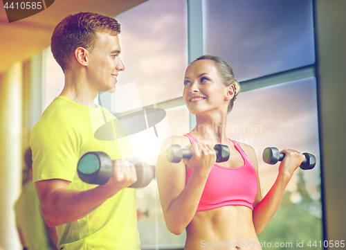 Image of smiling man and woman with dumbbells in gym