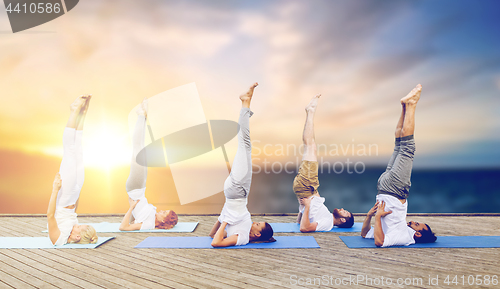 Image of people doing yoga shoulderstand on mat outdoors
