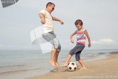 Image of Father and son playing football on the beach at the day time.