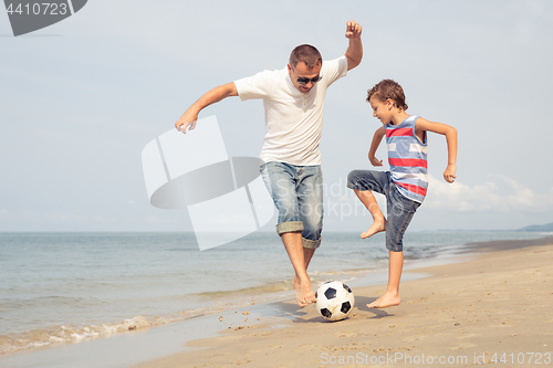 Image of Father and son playing football on the beach at the day time.