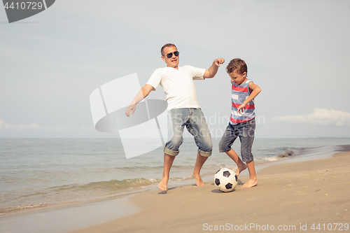 Image of Father and son playing football on the beach at the day time.