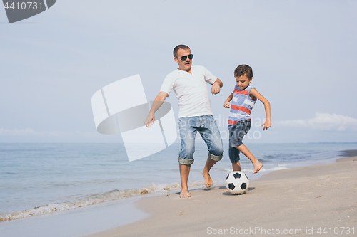 Image of Father and son playing football on the beach at the day time.