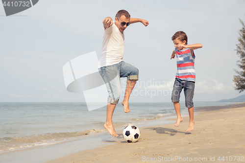 Image of Father and son playing football on the beach at the day time.