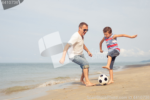 Image of Father and son playing football on the beach at the day time.